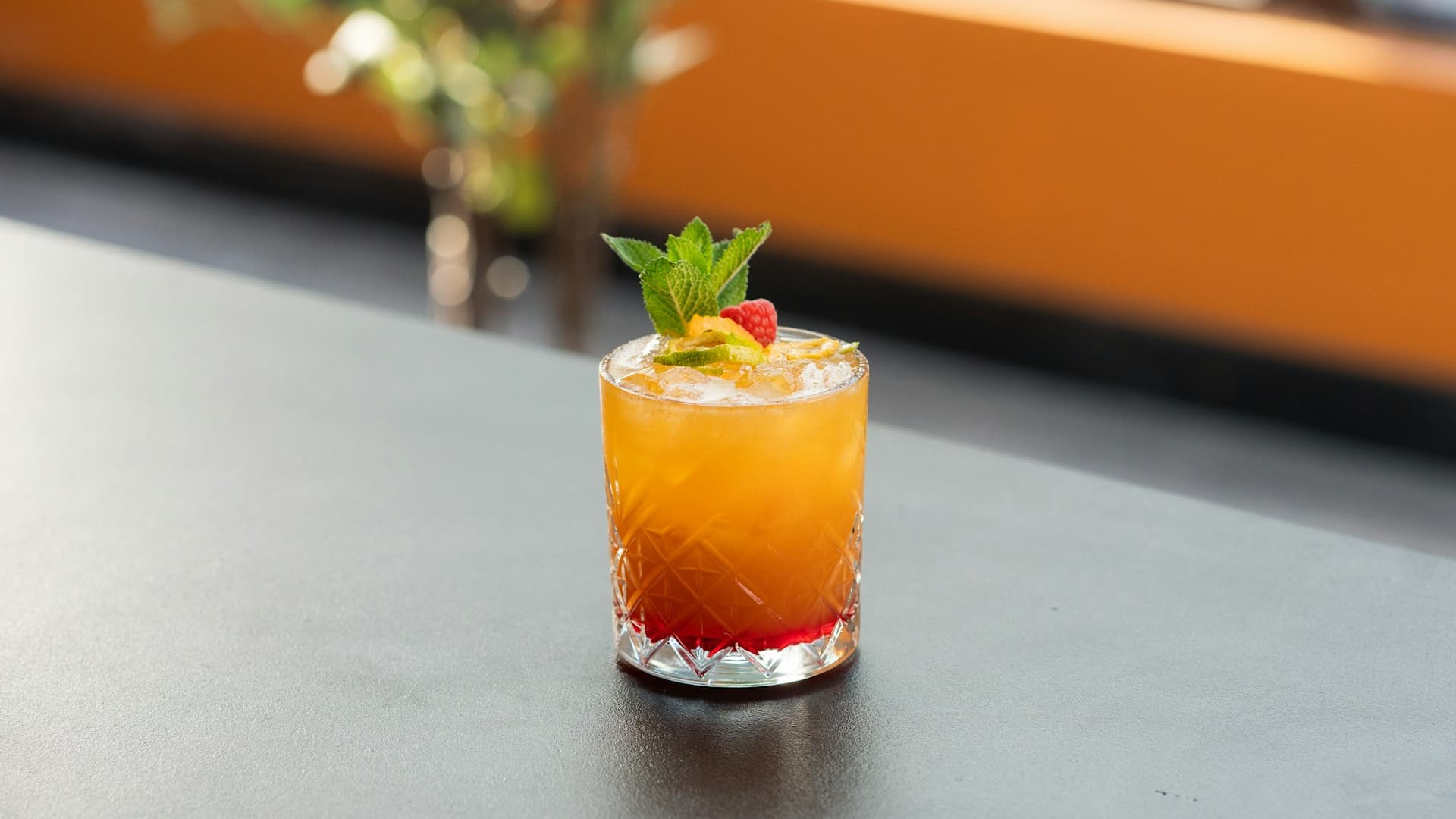 A glass of yellow-orange mule drink with mint and raspberry garnish standing on a dark counter